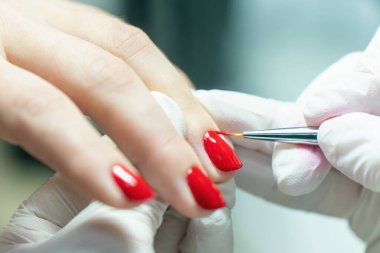 Manikür süreci, manikürcü müşterinin tırnaklarına kırmızı oje sürüyor..