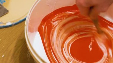 Bir işçinin eli beyaz boyayla kırmızı boyayı plastik kovada karıştırır.