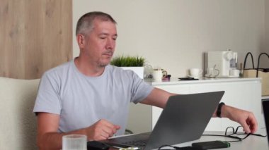 Dizüstü bilgisayarda çalışan bir adam daha iyi görmek için gözlük takar.