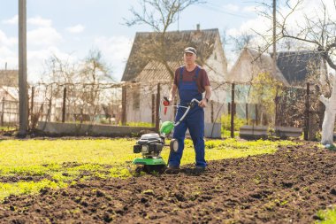 Bahçedeki bir çiftçi araziyi motorlu ekiciyle ya da dümenciyle işliyor, toprağı ekin ekmeye hazırlıyor..