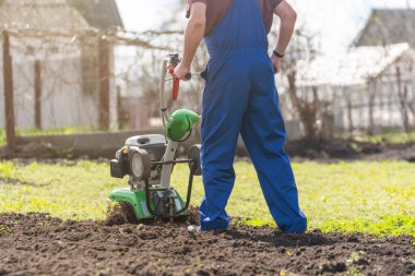 Tarımla uğraşan bir adam sebze ekimi için ekiciyle toprağı sürüyor..