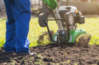 Bahçedeki bir çiftçi araziyi motorlu ekiciyle ya da dümenciyle işliyor, toprağı ekin ekmeye hazırlıyor..