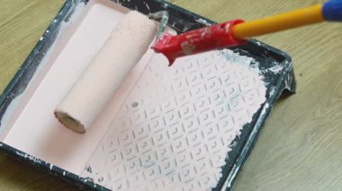 Bir işçi, plastik bir tepsiye sararken bir silindiri boyaya batırır.