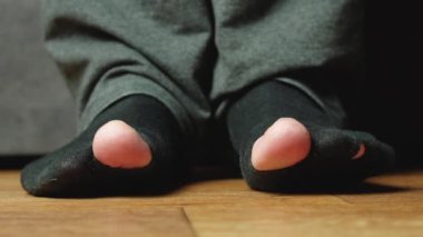 Ayak parmaklarında delikler olan eski siyah çoraplı bir adamın ayakları.