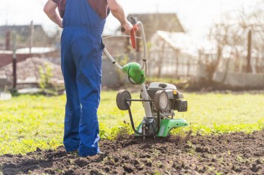 Bahçedeki bir çiftçi araziyi motorlu ekiciyle ya da dümenciyle işliyor, toprağı ekin ekmeye hazırlıyor..