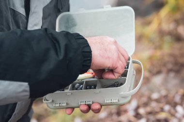 Balıkçının elleri çeşitli yem ve olta iğneleriyle dolu plastik bir kutu tutuyor..