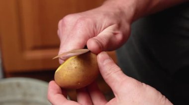 Erkek elleri mutfakta mutfak bıçağıyla patates soyarken patatesleri pişirmek için hazırlıyor.