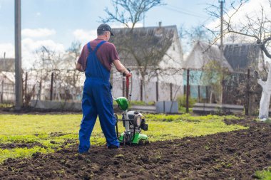 Tarımla uğraşan bir adam sebze ekimi için ekiciyle toprağı sürüyor..