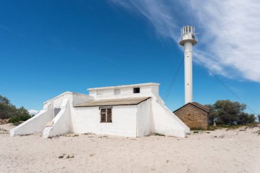 Lighthouse on Dzharylhach Island and a small white building on a sandy beach. clipart