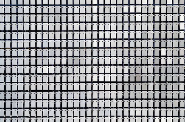 Metal plakalar özgürce asılı ve rüzgarda sallanıyor. Modern bir binanın kinetik cephesi..