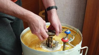 Bir işçi, pas ve mineral yataklarıyla kaplı bir elektrikli kazanın ısıtma elementini elinde tutar. Kazan bakımı ve onarımı
