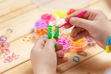 Çok renkli lastik bantlarla bilezik ören bir kızın elleri. Parmaklarının iyi motor becerilerinin gelişimi.