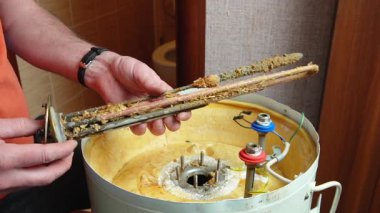 Bir işçi, pas ve mineral yataklarıyla kaplı bir elektrikli kazanın ısıtma elementini elinde tutar. Kazan bakımı ve onarımı