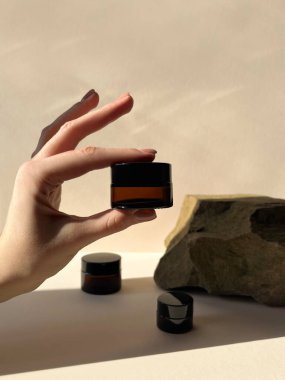 Woman holding jar of face cream on beige background, closeup