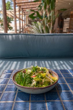 Mavi bir masa ve koltukta Sezar salatasının mutfak fotoğrafı.