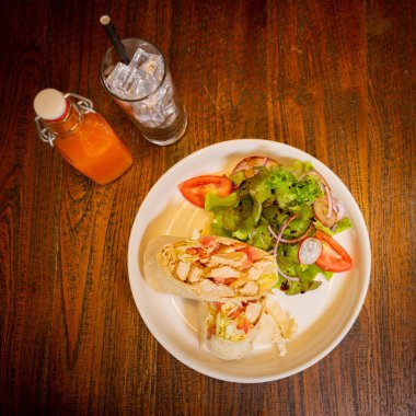 Kahvaltının en üst görüntüsü tabakta, tortilla ve yanında salata ile. Burrito kısmen açık et ve sebzeler dahil, arka plan ise ahşap bir masa.