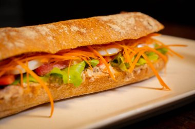 Sandviç yakın çekim, tonbalığı, domates, marul, havuç ve ahşap arka planda izole edilmiş sos ile babguette