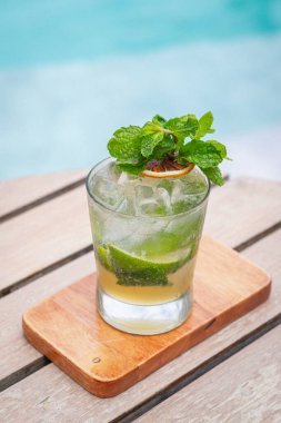 Bardakla süslenmiş mojito kokteyli. Bir dilim kurutulmuş limon ve bir havuzun önündeki tahtadan yapılmış nane yapraklarıyla süslenmiş.