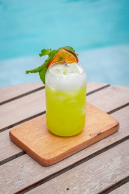 Midori ekşi kokteyli dilimlenmiş limon ve nane yaprakları bir havuzun önünde ahşap tahtalar üzerinde