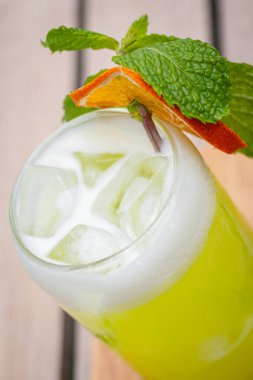 Yüksek açılı atış, Midori ekşi kokteyli dilimlenmiş limon ve nane yapraklarıyla havuzun önündeki tahta kalaslarda.