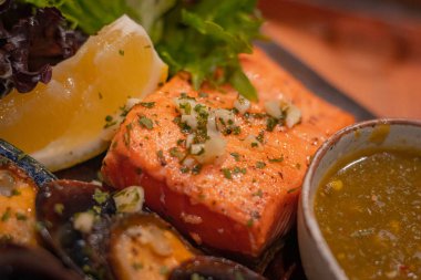 Izgara somon ve sebze, ahşap levhada küçük bir kase deniz ürünleri sosu.