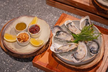 Üst manzara, buzda taze istiridye ve yeşil otlarla süslenmiş yuvarlak tabakta kızarmış soğan, deniz ürünleri sosu ve kırmızı biber ezmesi.