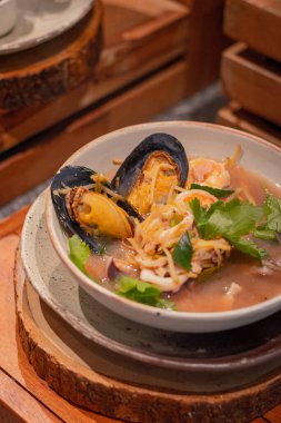 Yüksek açı, Tayland çorbası, Tayland otları ve deniz ürünleri kasede, ahşap servis tahtasının üzerinde. Tayland yemeğinin adı 