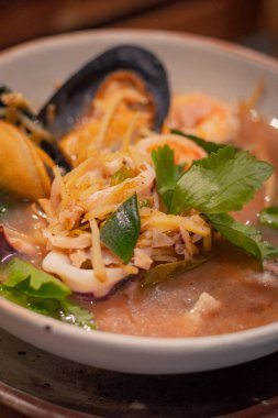 Yaklaş, Tayland baharatlı Tayland çorbası. Tayland otları ve deniz mahsulleri kasede. Tahta servis tahtasının üzerinde. Tayland yemeğinin adı 