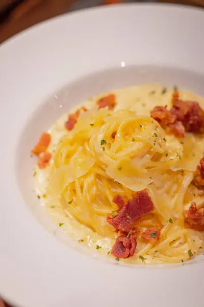 Yaklaş, domuz pastırmalı spagetti Carbonara, kremalı yumurta sarısı ve tabakta grana padano, ahşap levhada..