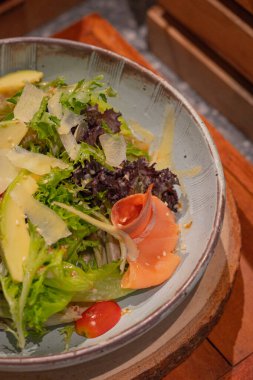 Yaklaş, roket salatası, füme somon, avokado, marul, domates ve İtalyan sosunu kaseye koy, ahşap servis tahtasına koy.