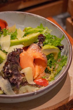 Yaklaş, roket salatası, füme somon, avokado, marul, domates ve İtalyan sosunu kaseye koy, ahşap servis tahtasına koy.