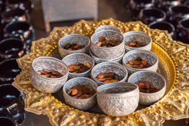 Küçük gümüş kaseler Tayland tapınağındaki altın tepside altın sikkelerle dolu.