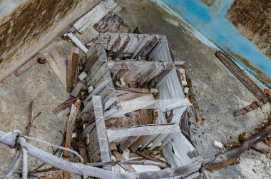 Çatlak ve kirli yüzeyi, kırık ahşap parçaları ve etrafa saçılmış enkazı olan ıssız bir sahne.