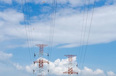 Kırmızı aksanlı iki uzun elektrik iletim kulesi mavi gökyüzü ve beyaz bulutlar