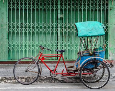 Eski bisiklet triportörü, Tayland 'da yeşil metal kepenkli bir duvarın yanına park edilmiş.