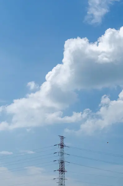 Kabarık beyaz bulutlarla dolu mavi gökyüzüne karşı yükselen yüksek bir elektrik hattı kulesi.