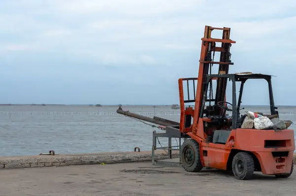 Kırmızı bir forklift yolun kenarındaki beton bir platformda duruyor.