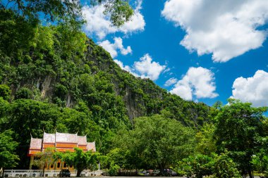Wat Tum Khao Chakan, Sa Kaeo, Tayland 'ın turuncu çatılı yemyeşil bitki örtüsüyle kaplı kayalık bir uçurum.