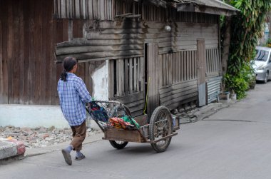 Chon Buri, Tayland - 8 Aralık 2018: Yıpranmış, ahşap bir binayla el arabası süren bir kadın