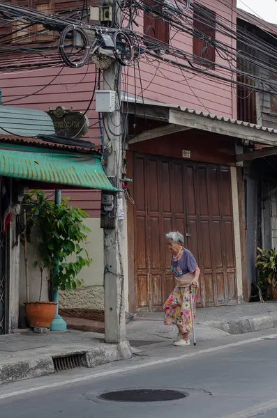 Chon Buri, Tayland - 8 Aralık 2018: Yaşlı bir kadın arka planda ahşap bir bina kapısı olan elinde bastonla caddede yürüyor