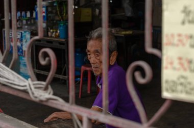 Chon Buri, Tayland - 9 Aralık 2018: Gri saçlı ve mor gömlekli yaşlı bir adam metal bir kapıdan görünen bir dükkanda oturuyor