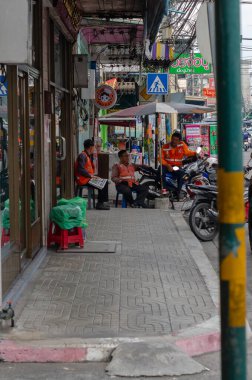 Chon Buri, Tayland - 9 Aralık 2018: 3 adam kaldırımda oturuyorlar, turuncu yelek giyiyorlar ve günün tadını çıkarıyorlar.