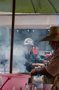 Chon Buri, Tayland - 9 Aralık 2018: Sıcak yemek pişirme alanında çalışan biriyle kalabalık bir açık hava ortamında bir sokak yemeği sahnesi
