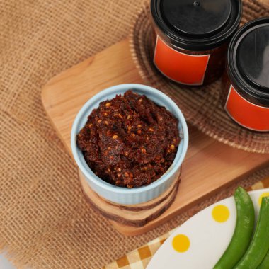 Tahta kesme tahtası ve turuncu etiketli kavanozlar üzerinde bir kase Tayland biberi ezmesi.