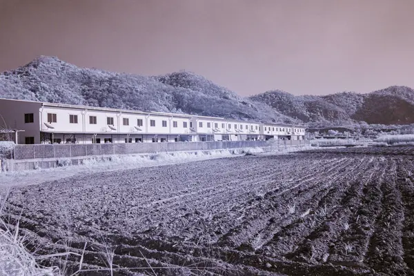 Kızılötesi fotoğrafçılık, arka planda dağlar olan bir manzara, orta zeminde bir sıra bina veya evler, ve ön planda ekilmiş bir tarla.