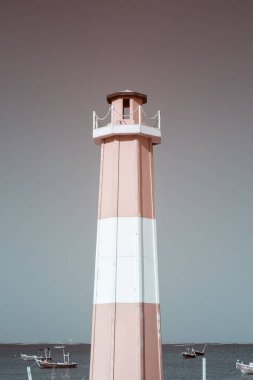 Kızılötesi fotoğraf, pembe ve beyaz çizgili uzun bir deniz feneri. Belirgin bir şekilde sakin bir denize karşı duruyor.