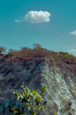 Az miktarda bitki örtüsü ve tek bir kabarık bulutu olan kayalık bir yamaç.