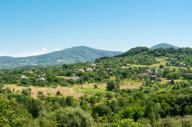 Bir dağ manzarasının ortasında yeşil bahçelerde boğulan bir köy berrak mavi bir gökyüzünün arka planına karşı