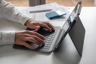 Still life. Studio shot of a man with a white shirt using a digital tablet, stylus, keyboard, screen, administrative paper, and a calculator