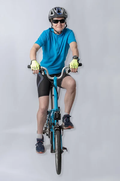 Studio shot detail of a woman dressed in a blue polo shirt, black shorts and a bicycle helmet, poses next to her blue folding bicycle